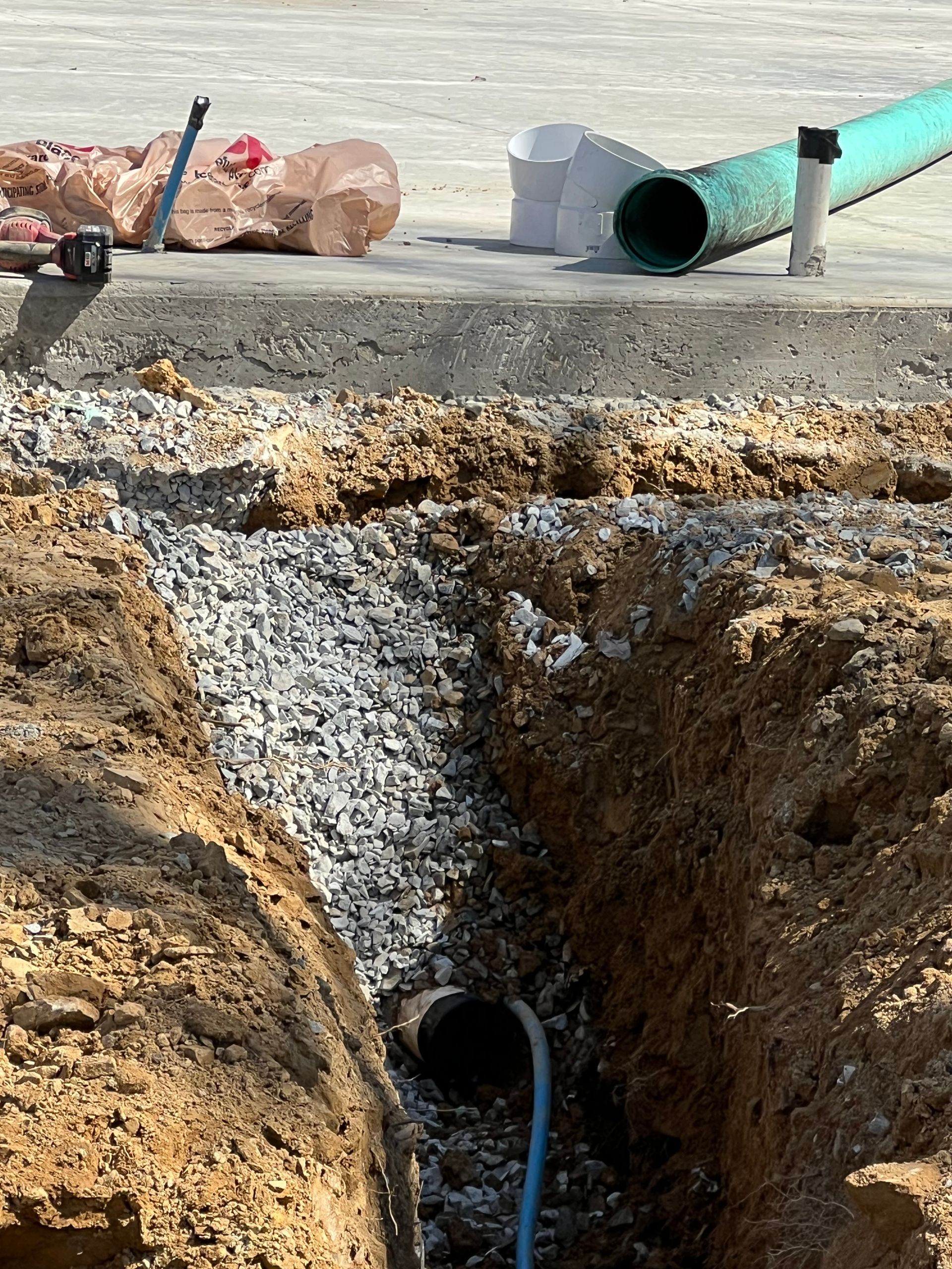 Trench with gravel and pipe, construction site. Green pipe on ground.