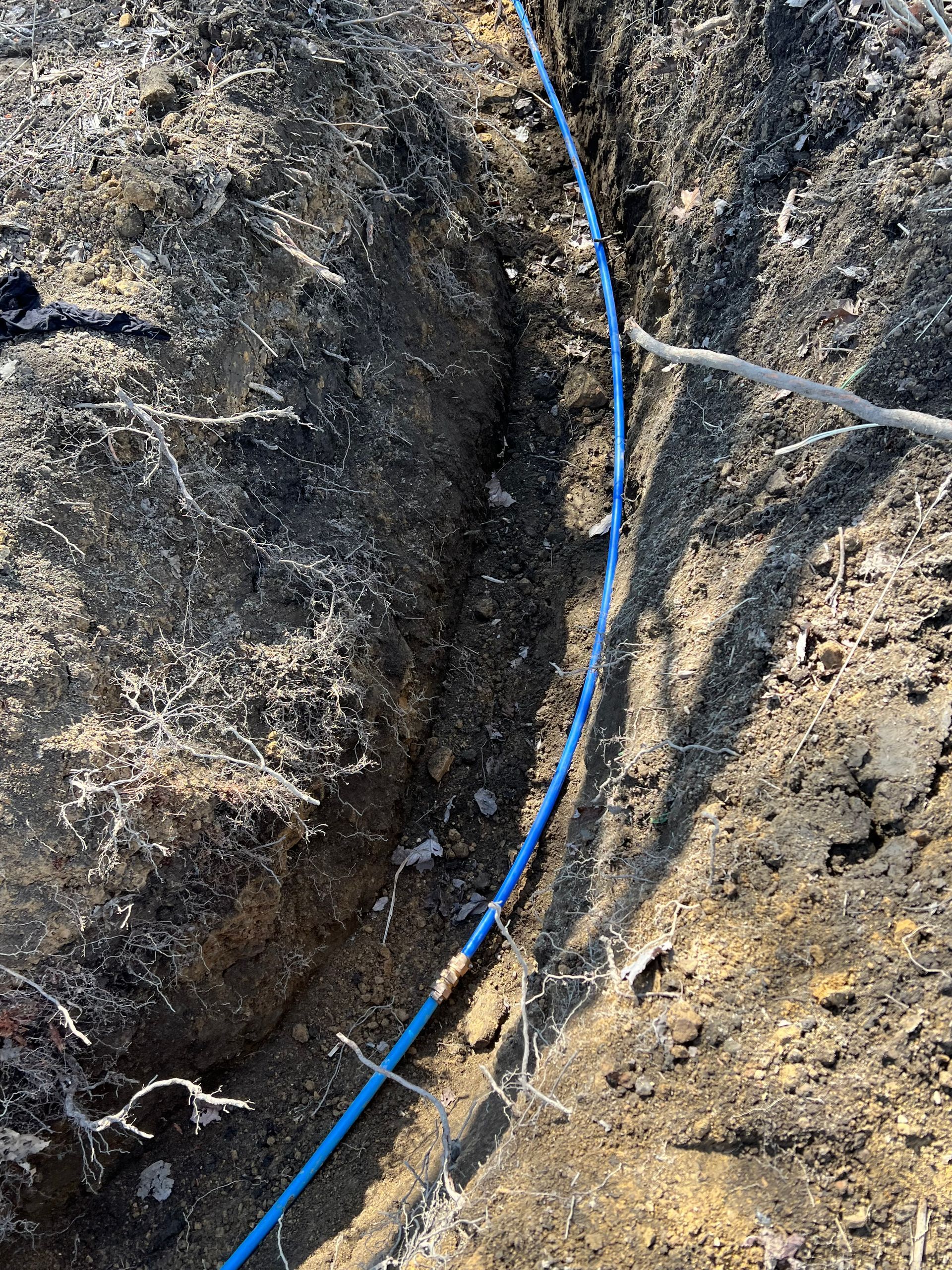Blue cable in a narrow trench in the ground.