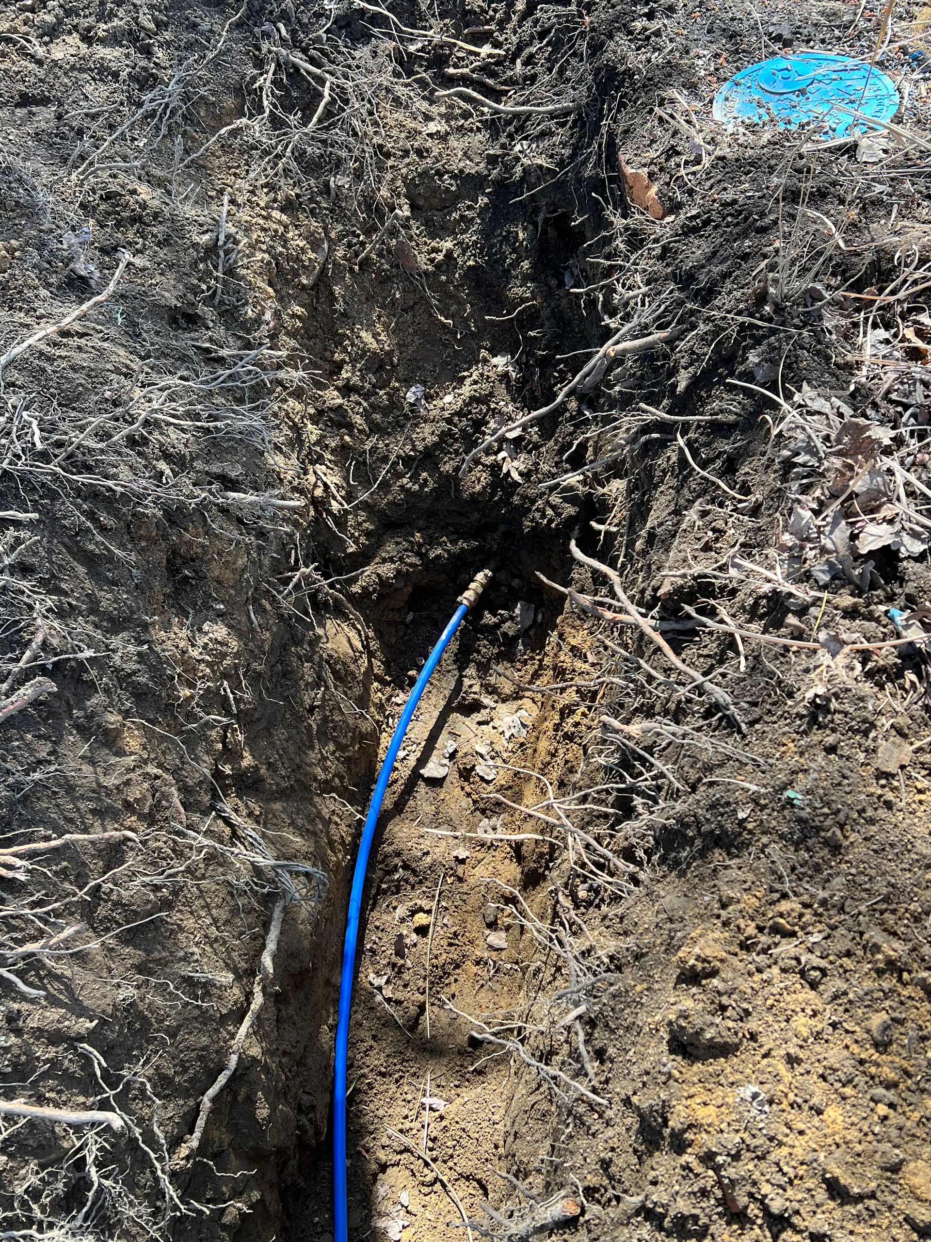 Blue cable emerging from a hole in brown soil. Blue marker in the background.
