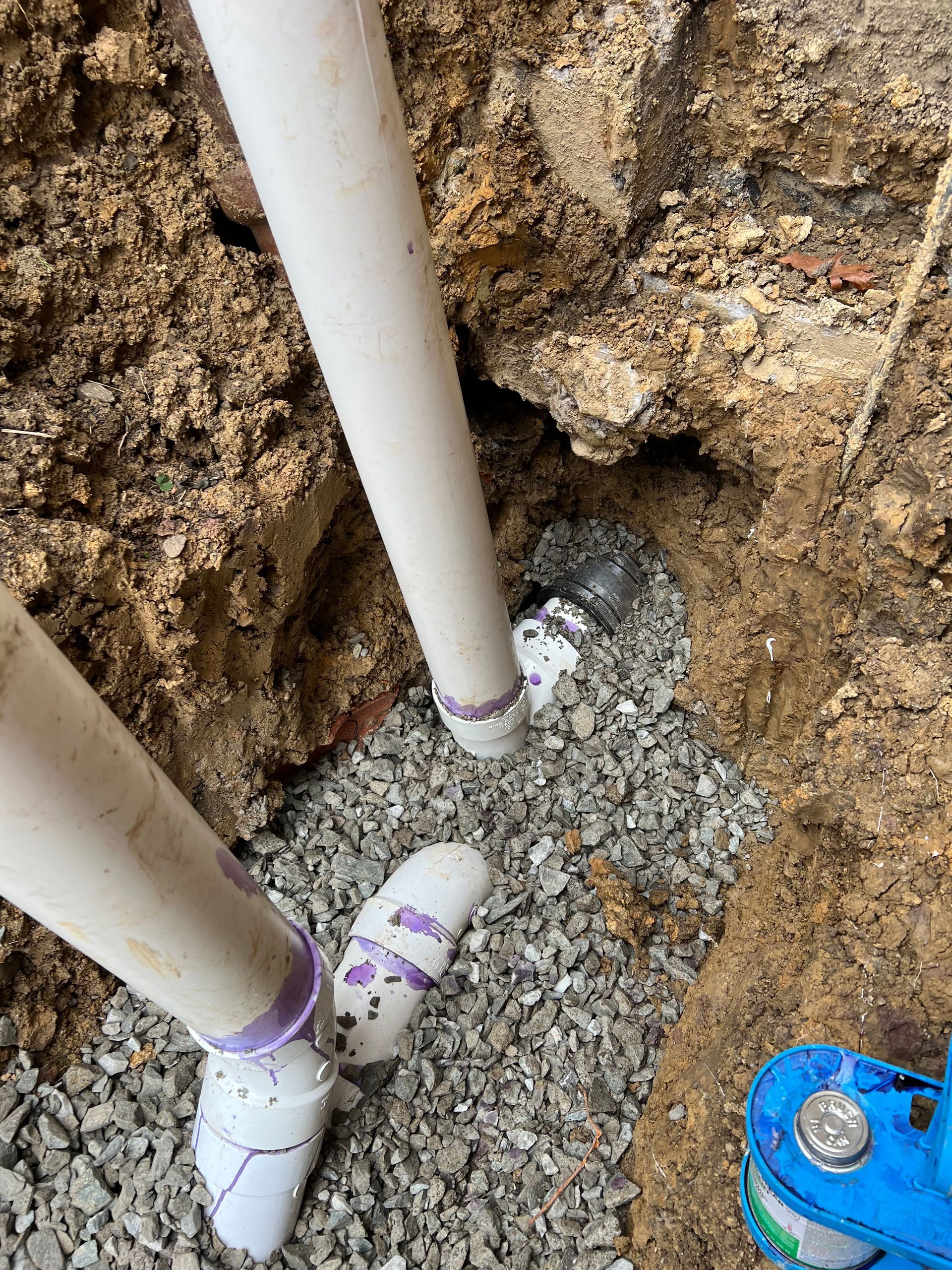 PVC pipes connected in a gravel-filled trench.