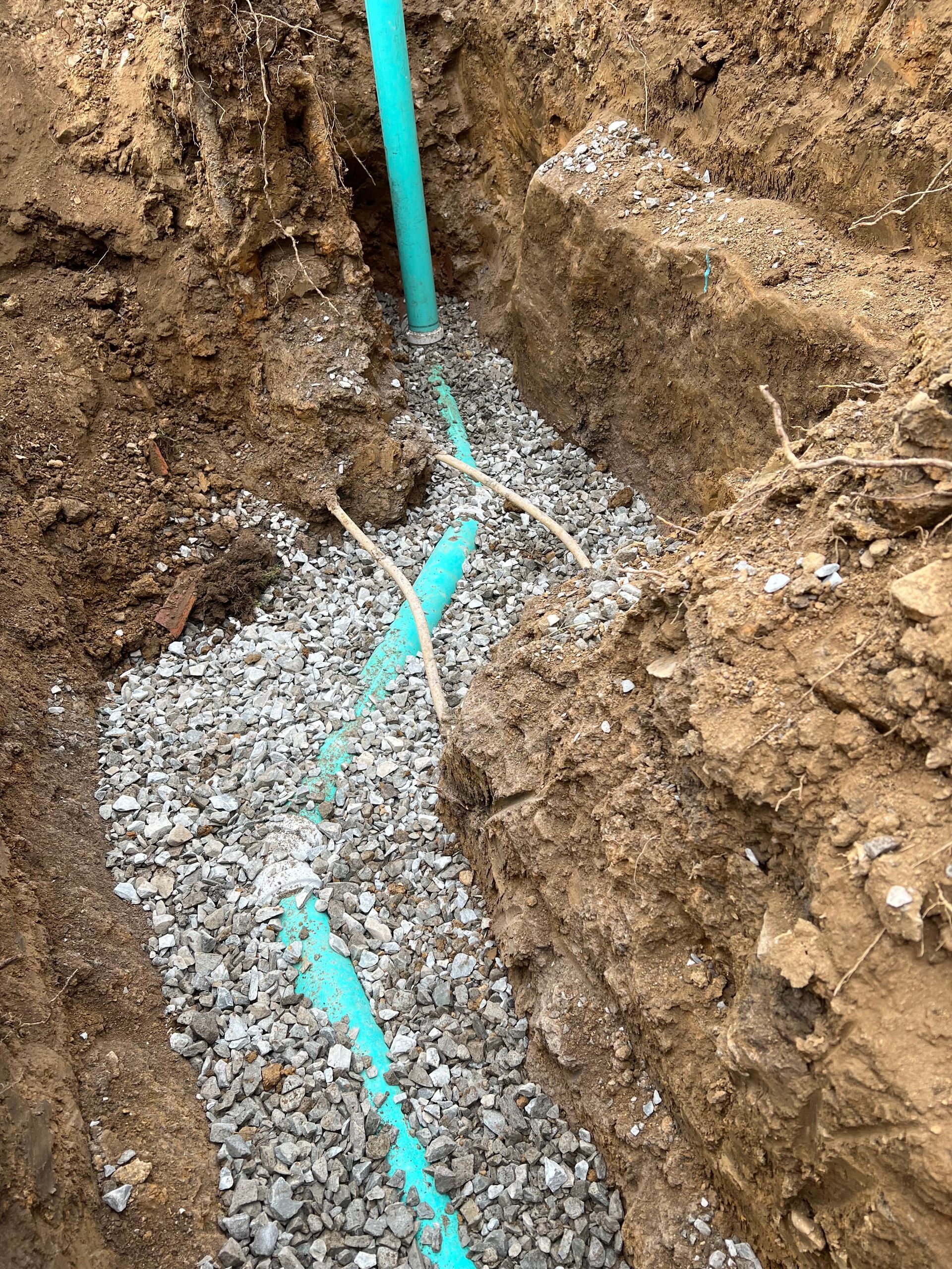 Blue pipes laid in a gravel-lined trench, surrounded by dirt.