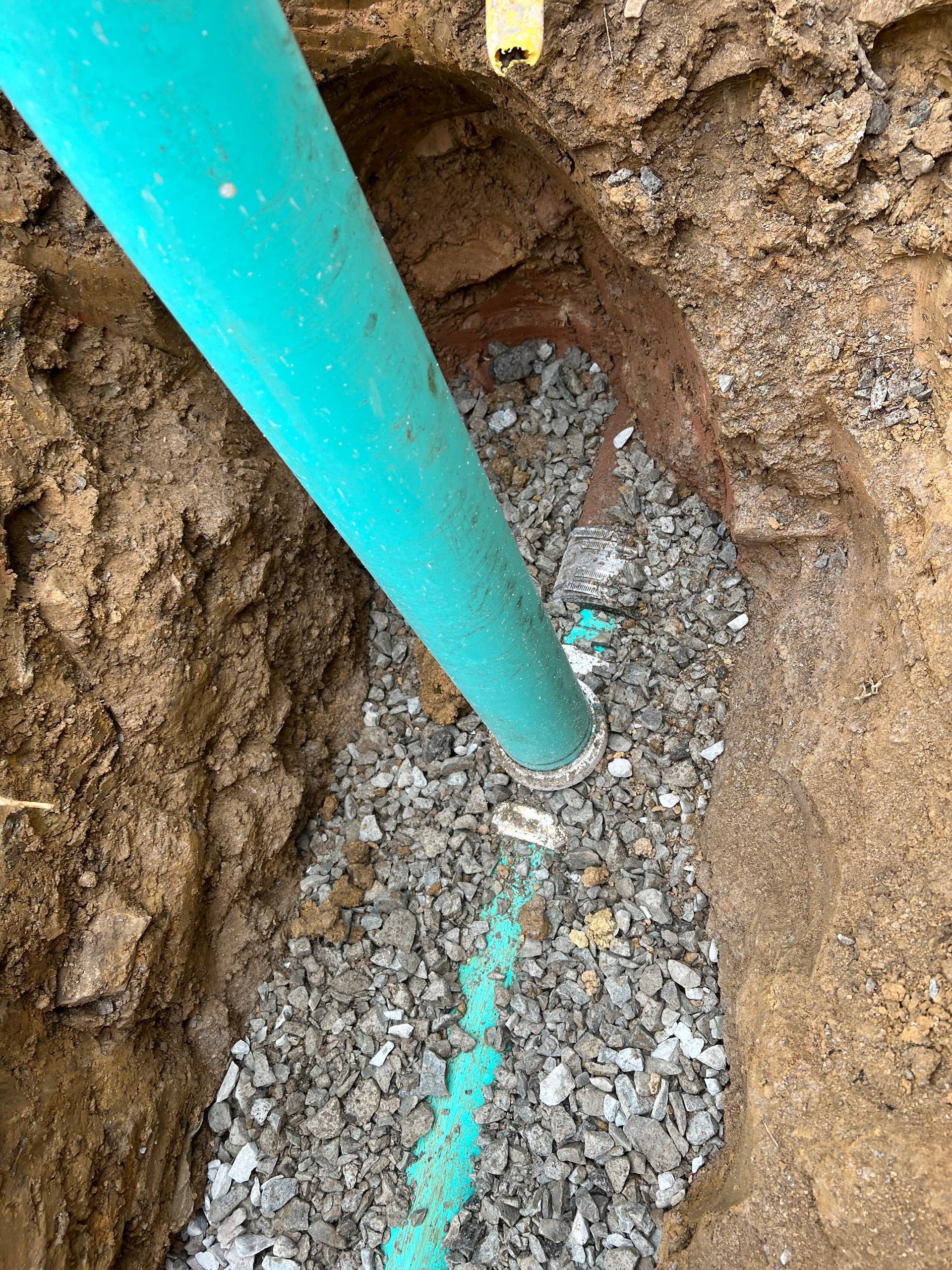 Blue PVC pipe in a trench filled with gravel, likely a water line installation.