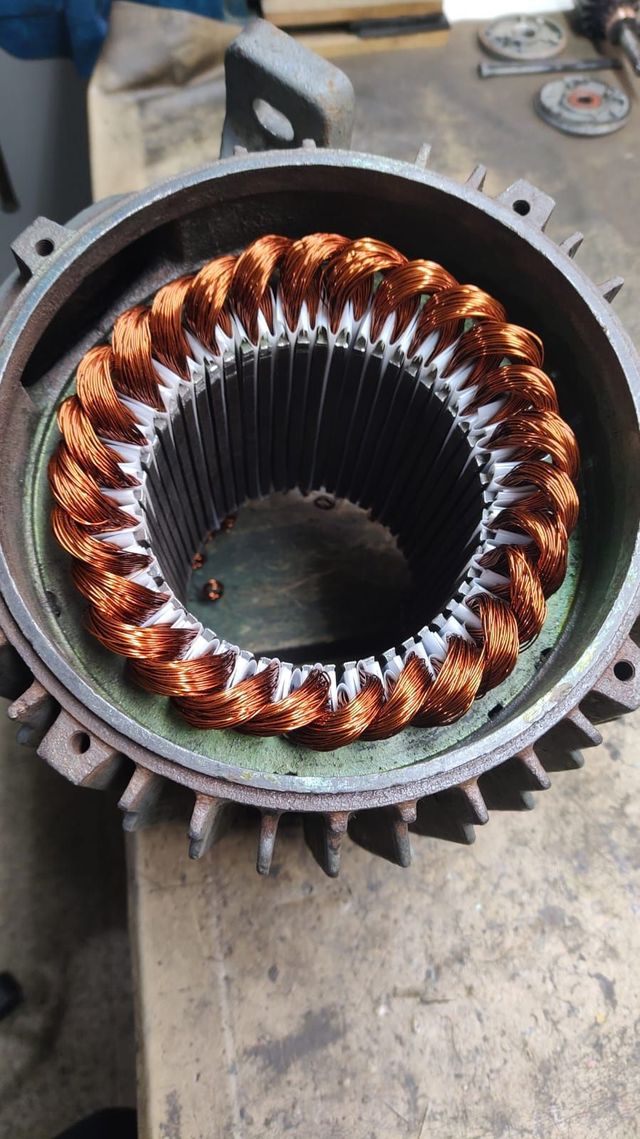 Bobinas de cobre dentro de la carcasa circular del estator de un motor eléctrico sobre un banco de trabajo.