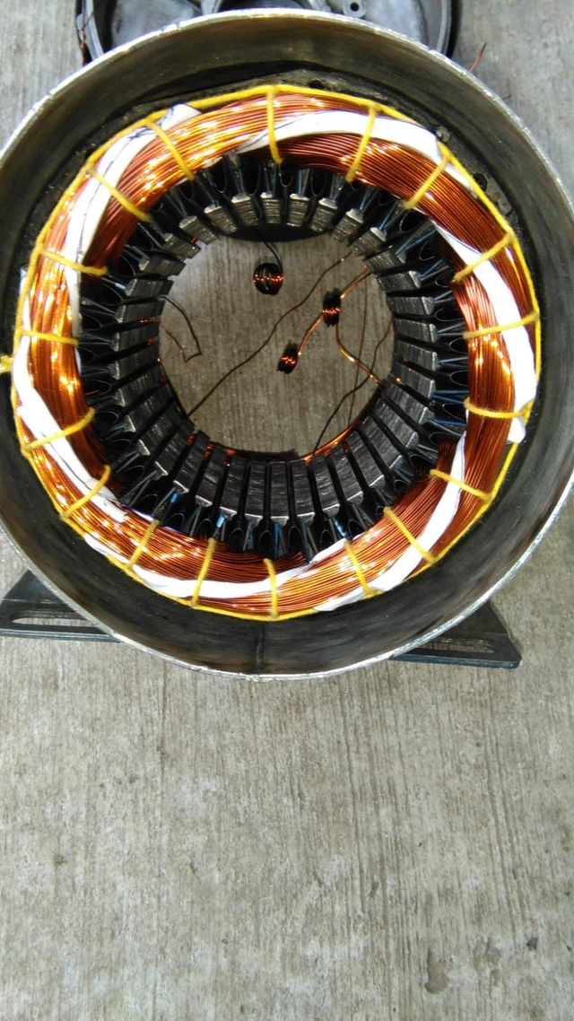 Vista superior de un estator de motor eléctrico circular con bobinados de cobre sobre un suelo de hormigón.