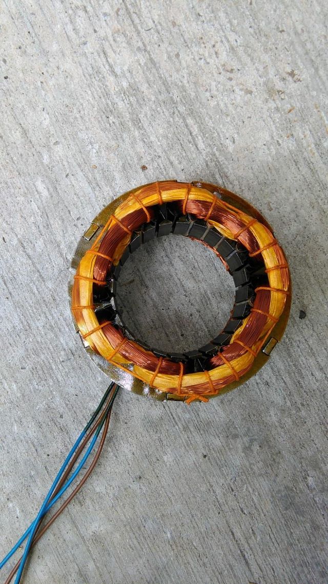 Bobina toroidal de alambre de cobre con aislamiento naranja sobre una superficie gris.