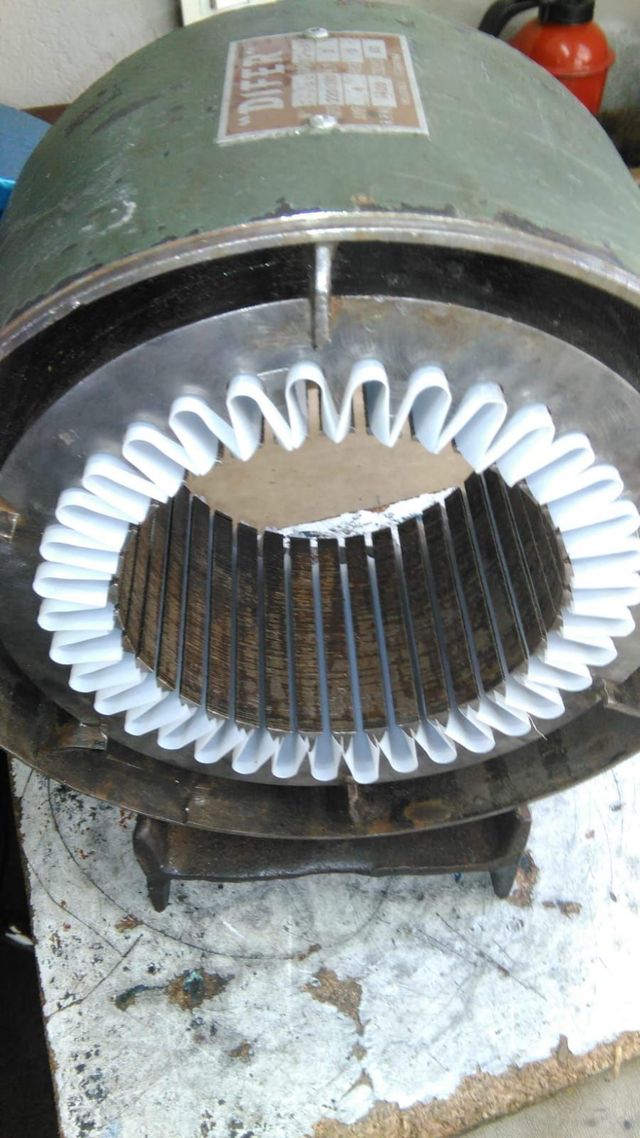Estator de motor eléctrico verde con bobinados de cobre blanco sobre un banco de trabajo.