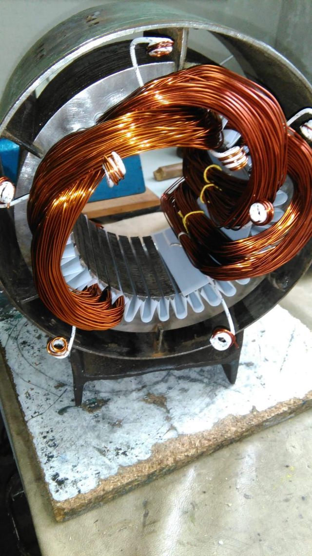 Cable de cobre enrollado alrededor del estator de un motor sobre una base blanca, con aletas de refrigeración metálicas visibles.