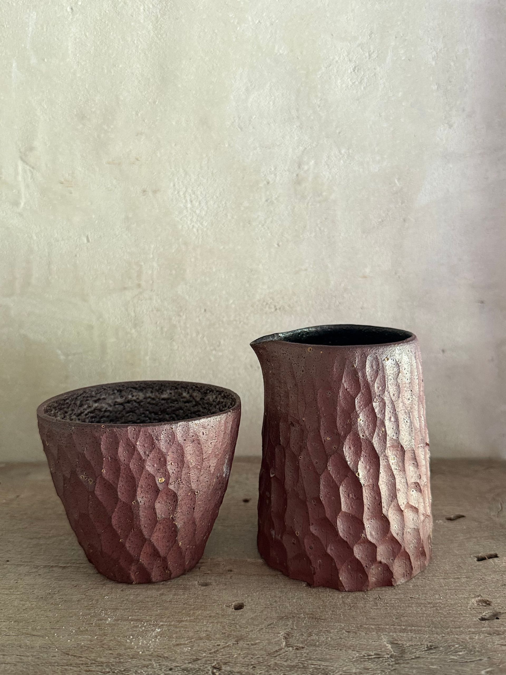 Two textured pink planters, one short and one tall, against a plain wall