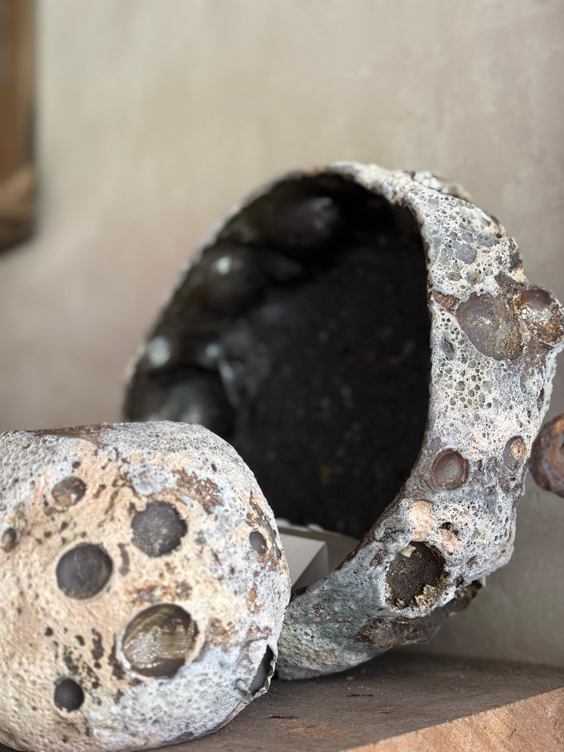 Two speckled, weathered ceramic vessels with dark interiors on a wooden surface