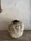 Small round, dirty stone or ceramic object sitting on a floor against a plain wall