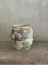 Small rustic ceramic jar with a white and gray mottled glaze on a concrete surface