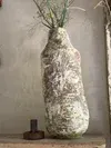 A large white cocoon-like hanging sculpture in a sparse room, with two small dark objects on the floor beside it.