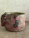 Pink metal bucket with worn floral paint and rust, sitting on a floor