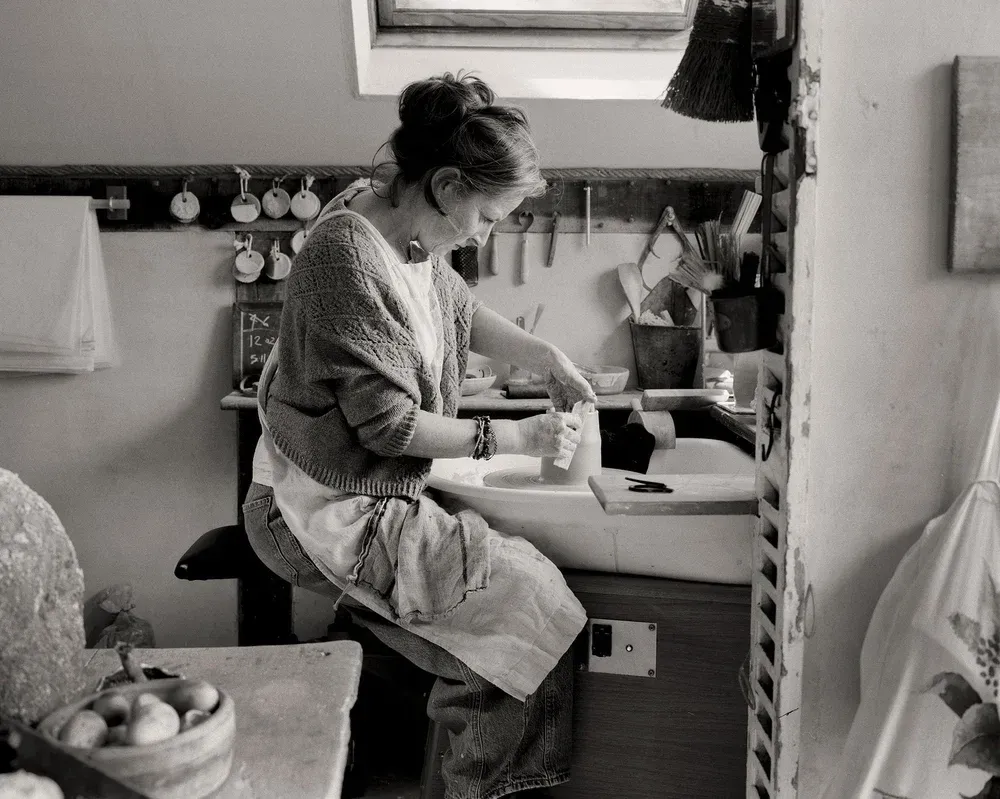 A woman is sitting at a table painting with a brush.