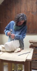 A woman is sitting at a table carving a statue.