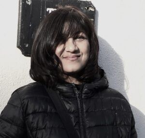 A woman in a black jacket is standing in front of a white wall.