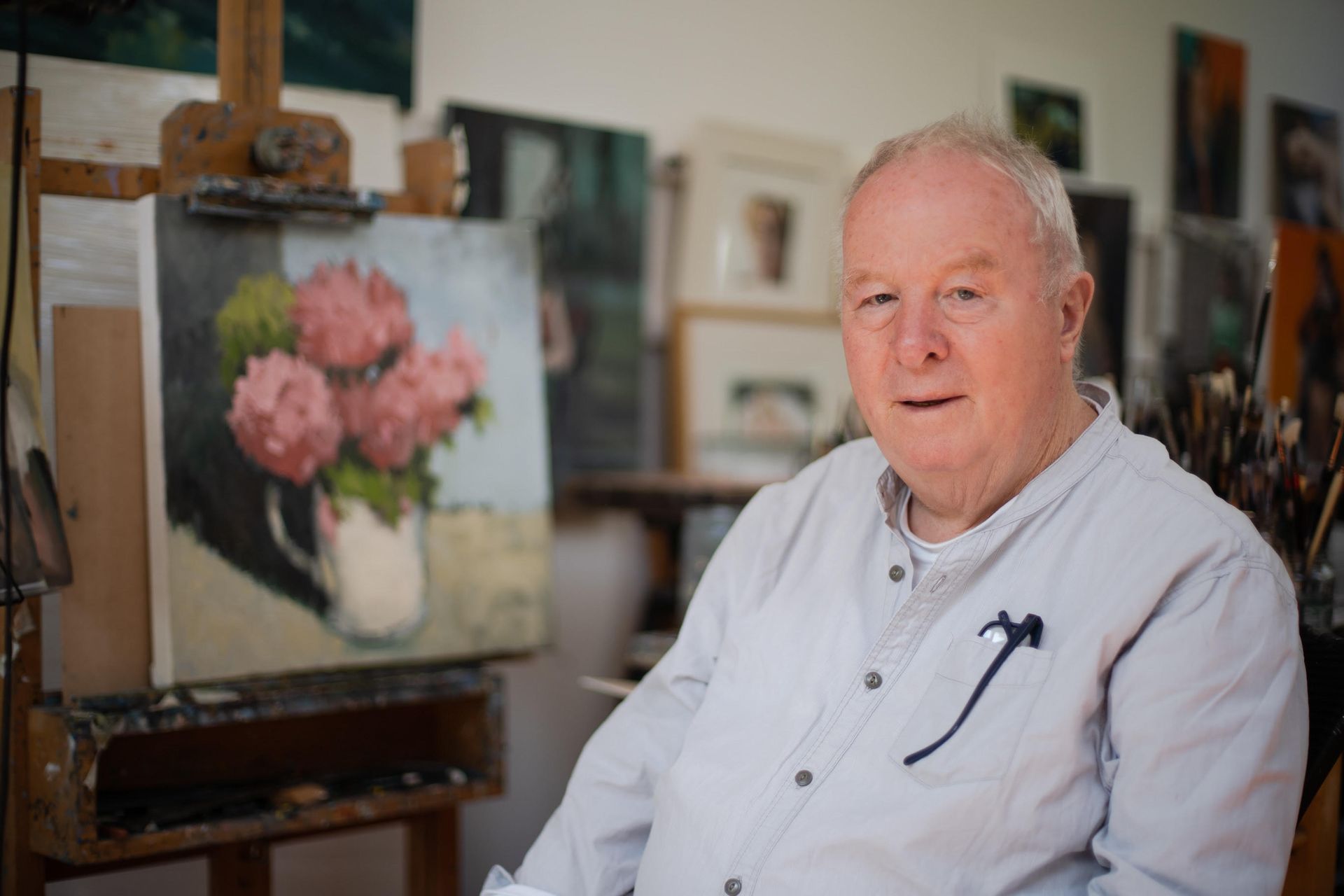 A man is sitting in front of a painting of flowers on an easel.