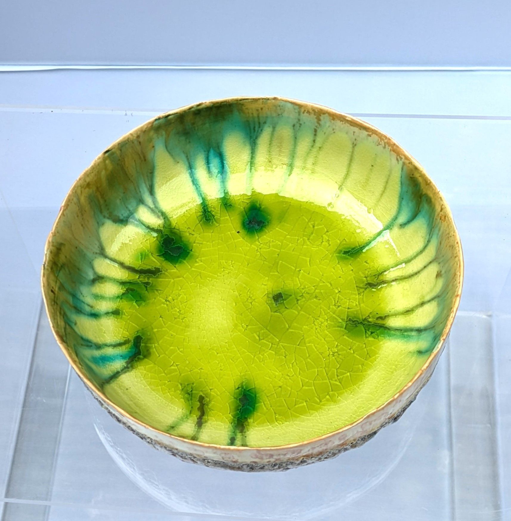 A green and yellow bowl is sitting on a clear display case.
