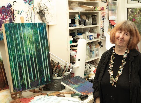 A woman is standing in front of a painting on an easel