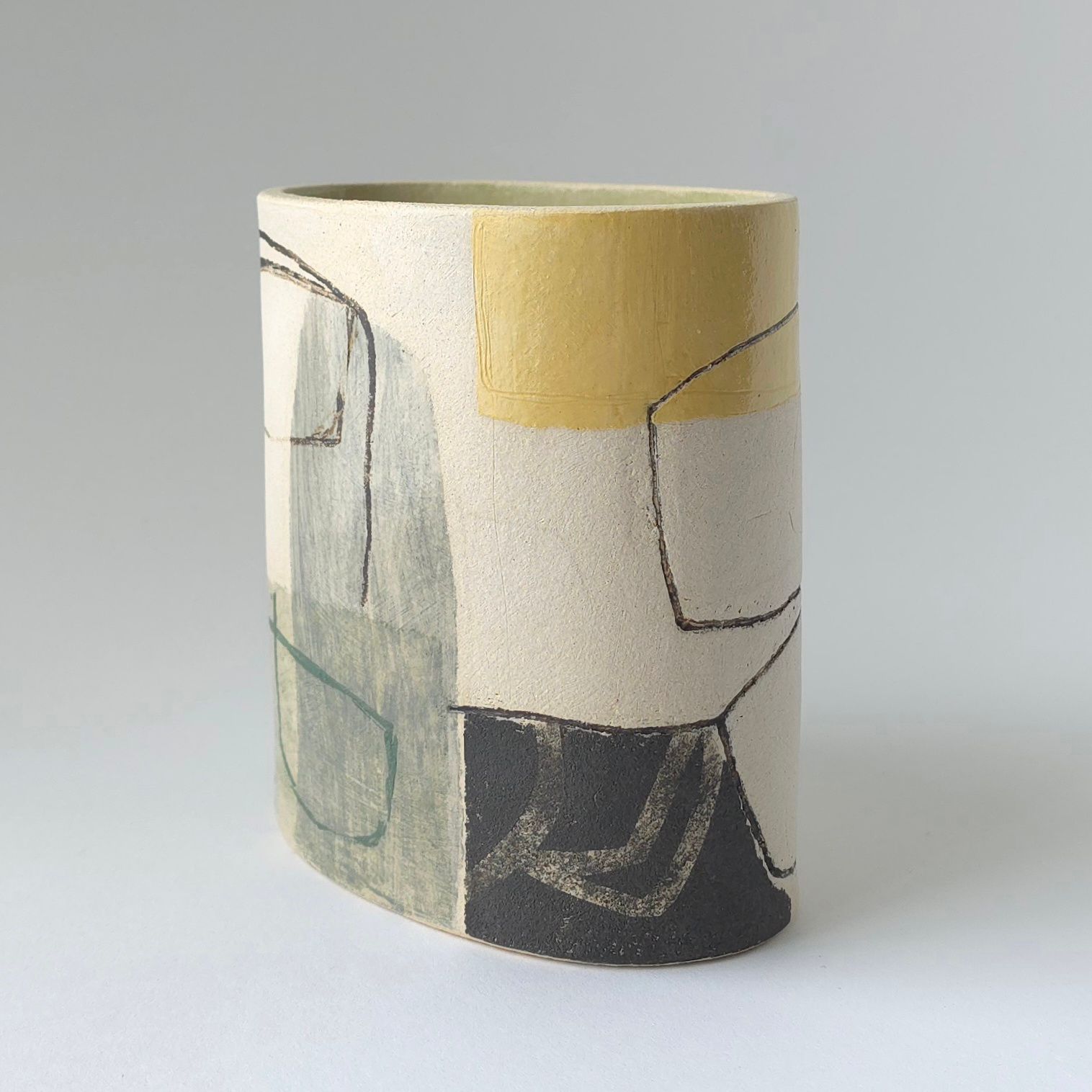 A tall, oval ceramic vase with a speckled cream surface, decorated with abstract black lines and blocks of yellow and blue.