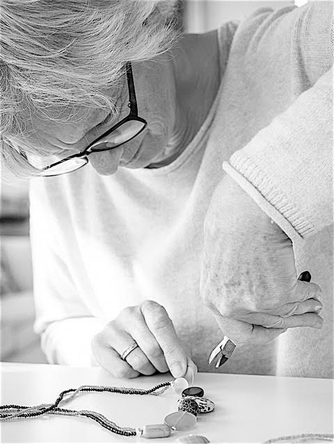 A woman wearing glasses is sitting at a table looking at a necklace.