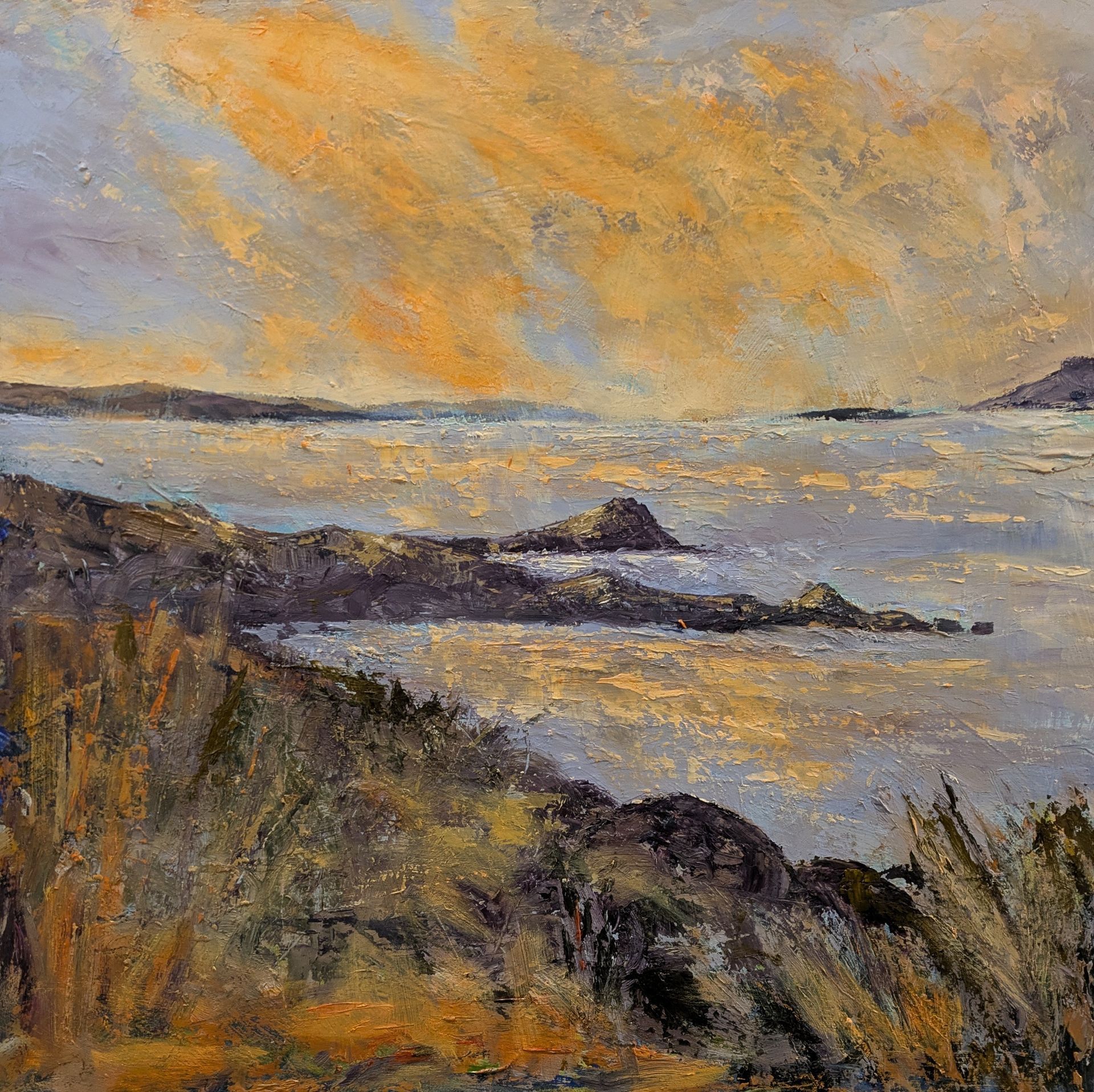 Coastal landscape with golden light reflecting on water and sky. Rocky shoreline in foreground.