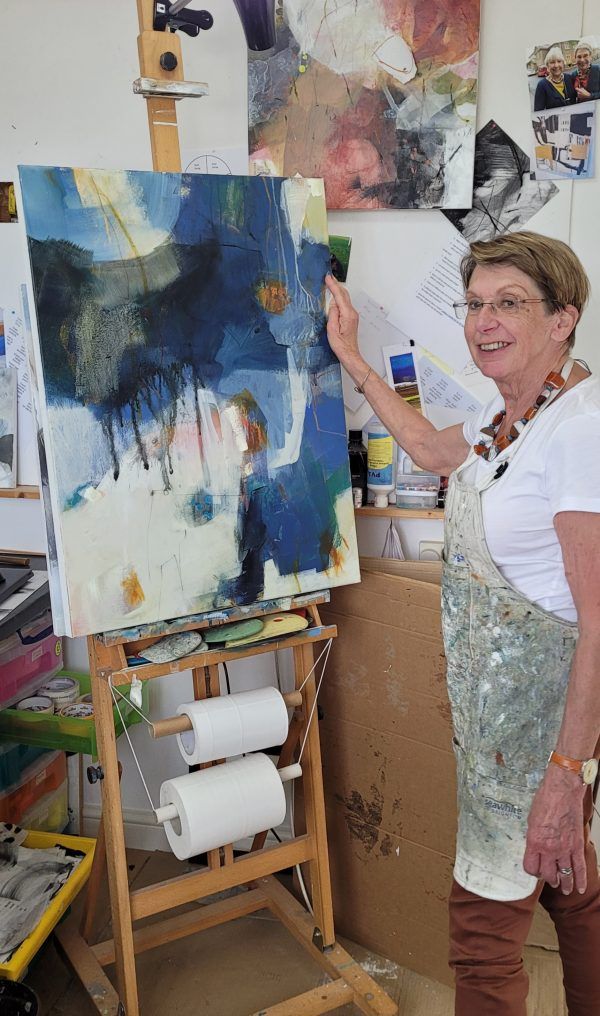 A woman is standing in front of an easel painting a picture.