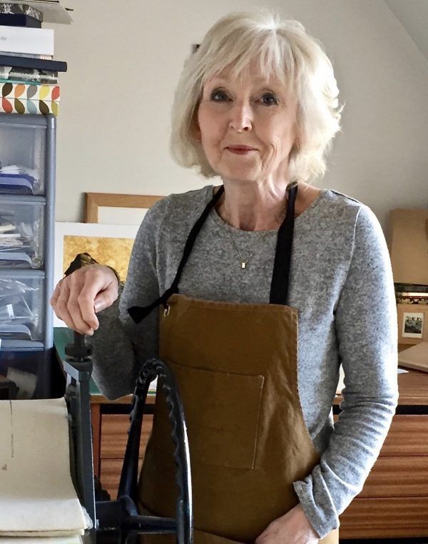 A woman wearing an apron is standing in front of a machine.