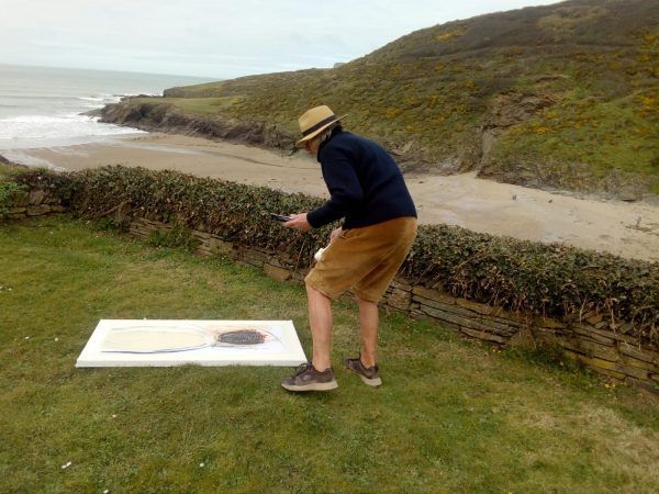 A man in a hat is standing on a grassy hill near the ocean.
