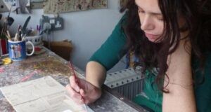 A woman is sitting at a table painting with a brush.