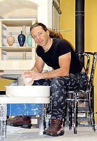 A man is sitting on a chair in front of a pottery wheel.