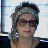 A woman wearing glasses and a headband is sitting in front of a window.