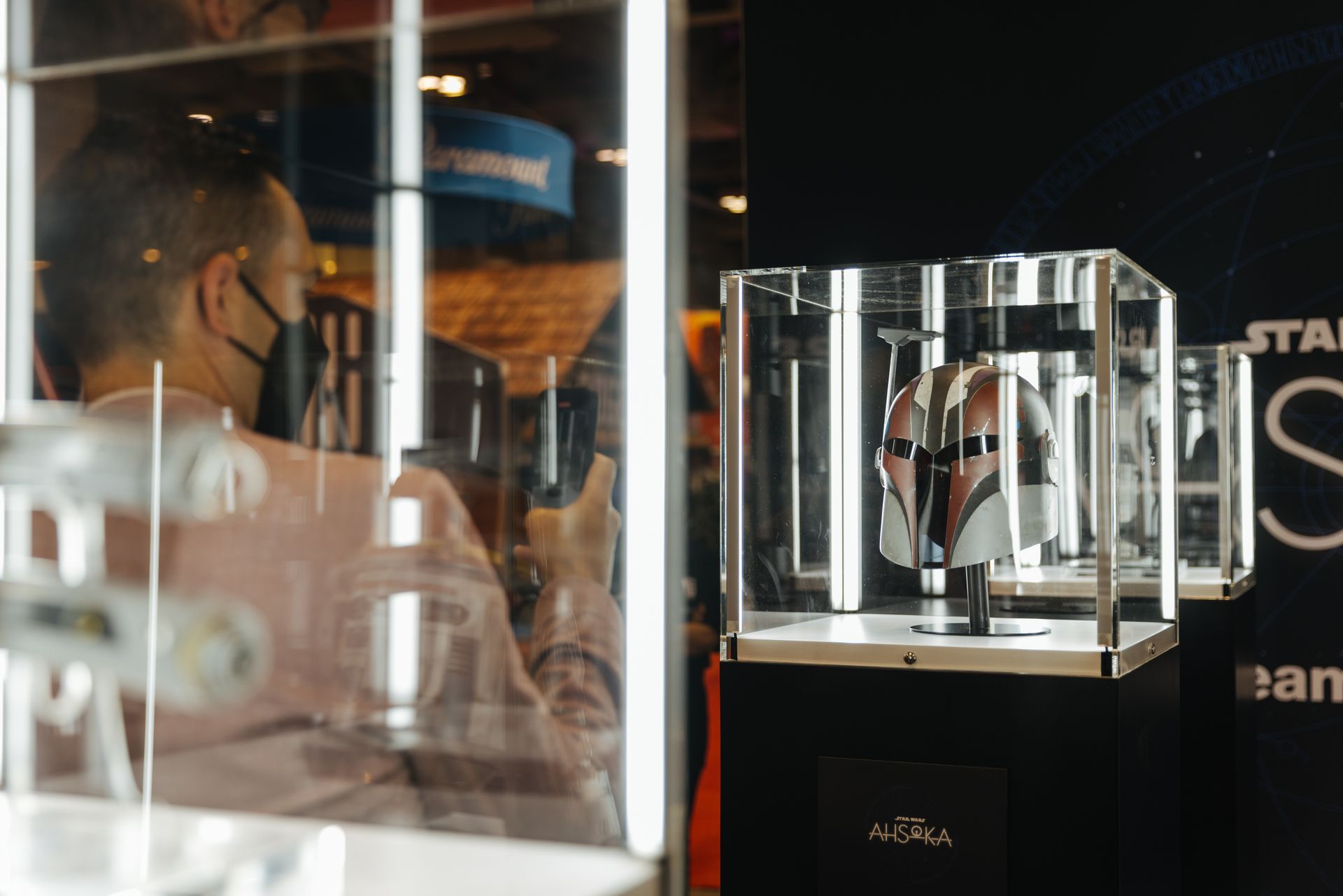 A man wearing a mask is looking at a star wars action figure in a glass case.
