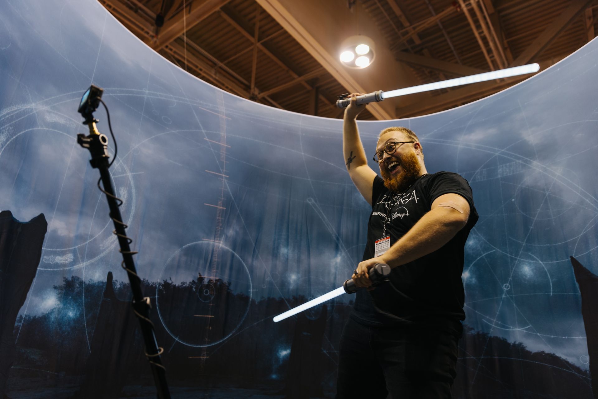 A man in a black shirt is holding two lightsabers in his hands.