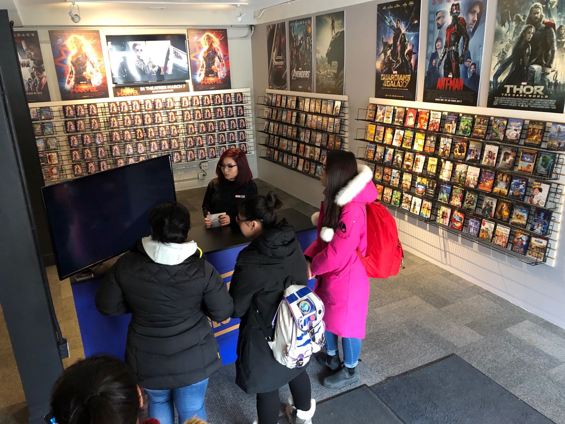 A group of people are standing in a room with posters on the wall at the Disney Captain Marvel event