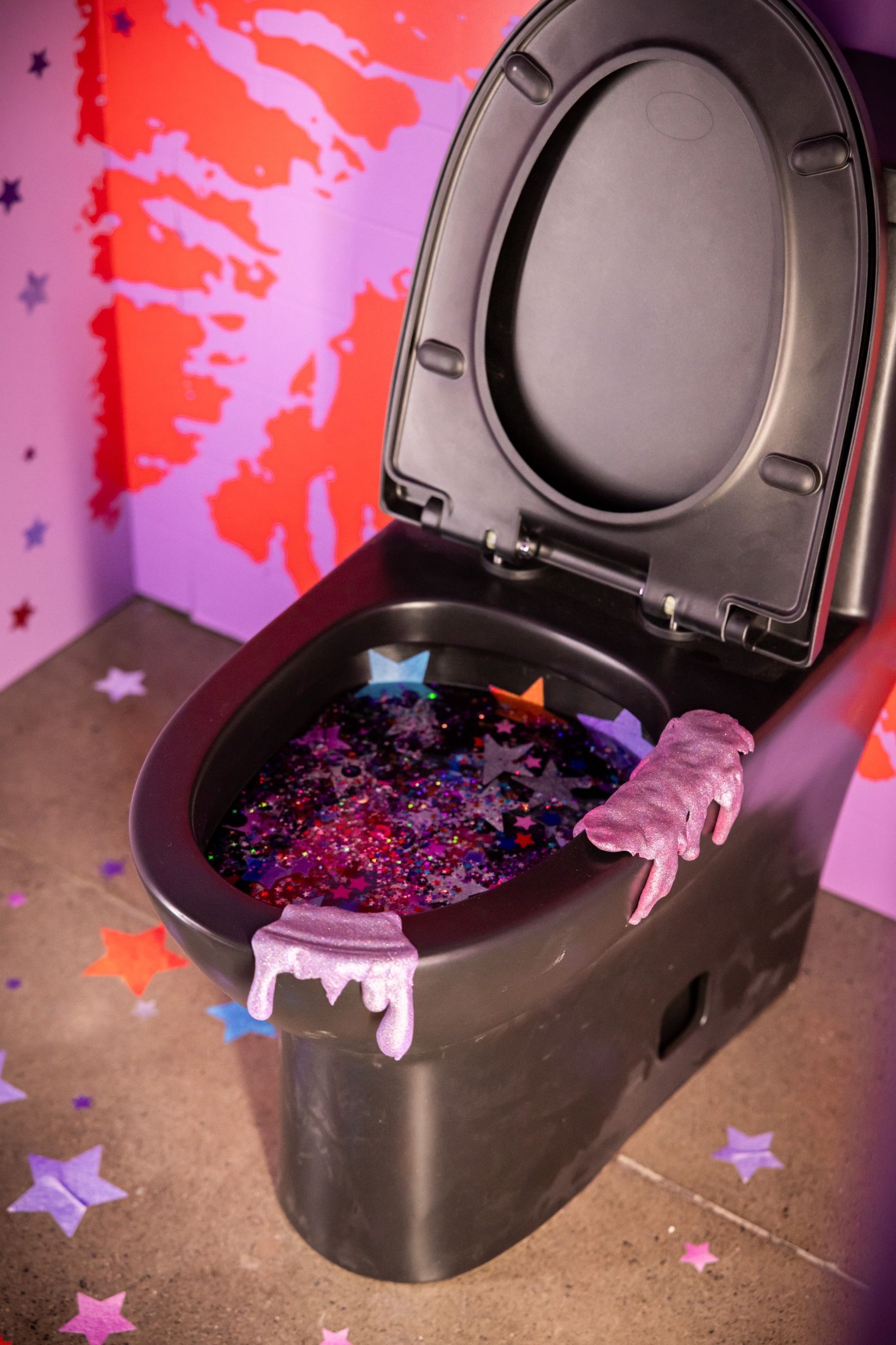 A black toilet is filled with purple glitter and stars.