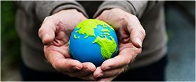 A pair of hands cupped together, gently cradling a small, blue and green model of the Earth.