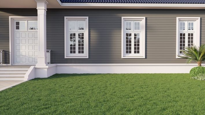 Une maison à l'extérieur gris avec une porte blanche, trois hautes fenêtres à encadrement blanc, un porche à colonnes et une pelouse verte.