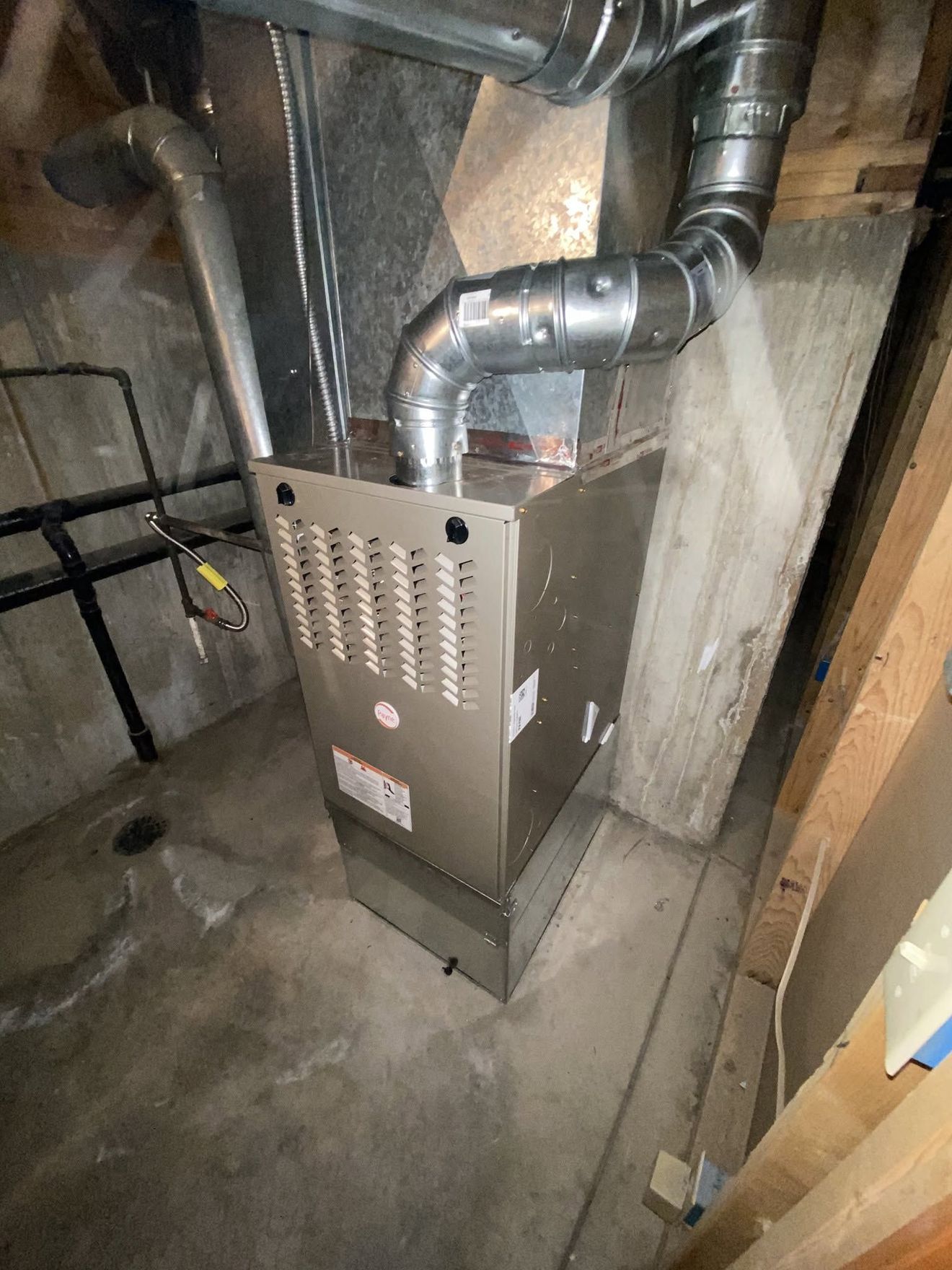 Basement furnace beside exposed silver ductwork and concrete walls