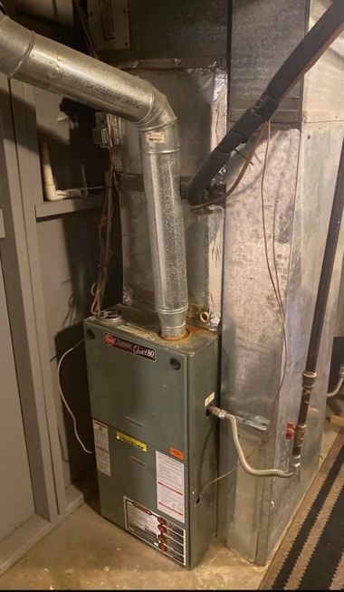 HVAC furnace and ductwork in a utility closet with metal pipes and insulation