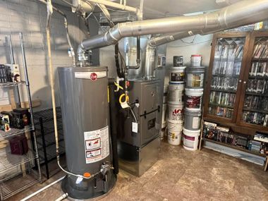 Basement utility room with water heater, furnace, vents, and shelves of stored supplies.