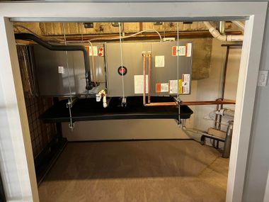 Basement utility room with furnace, water heater, exposed pipes, and concrete floor