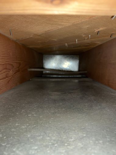 Interior of a wooden air duct or crawl space, with a bright opening at the far end.