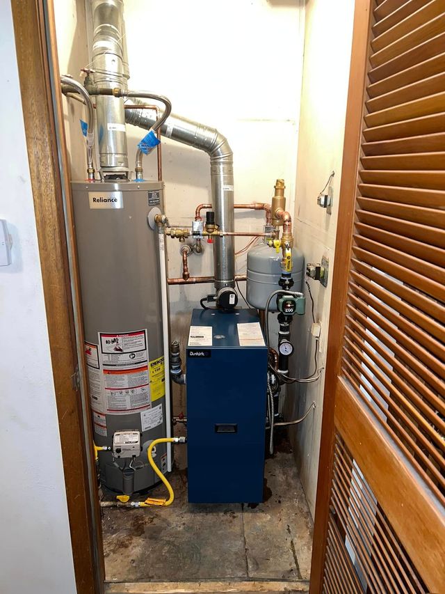 Utility closet with a boiler, pipes, and a blue HVAC unit beside wooden louvered doors.