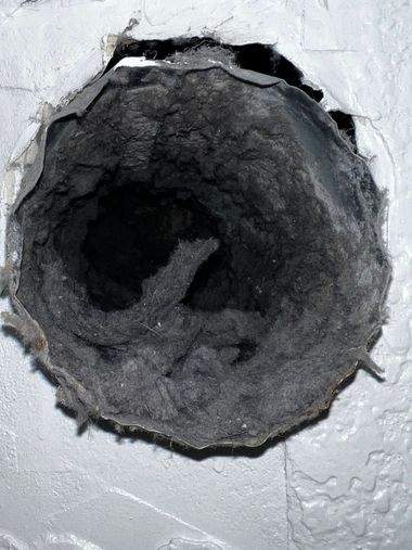 Close-up of a dark circular hole in a white wall or ceiling surface with rough, crumbling edges