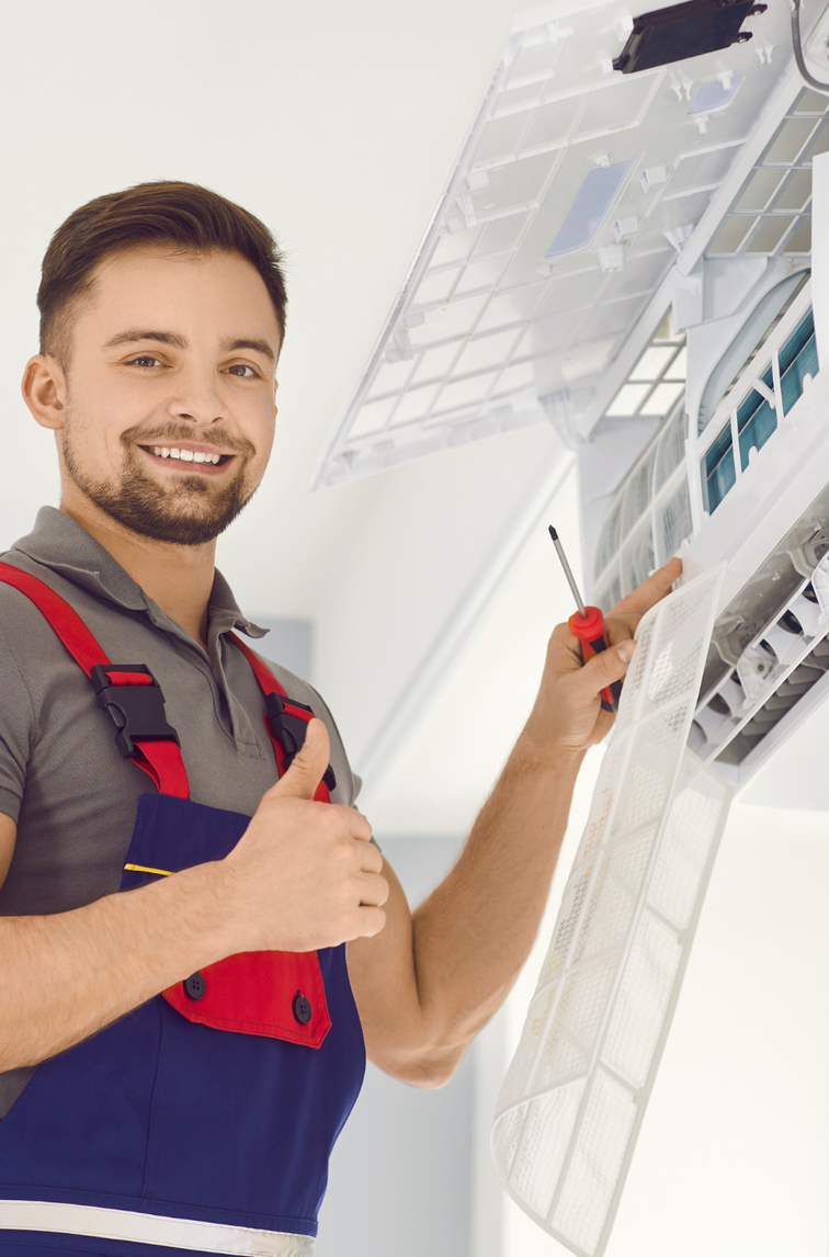 Technician in red and navy uniform installing ceiling tiles with a screwdriver indoors.