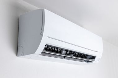 Wall-mounted white air conditioner on a light-colored wall, angled downward with open vents