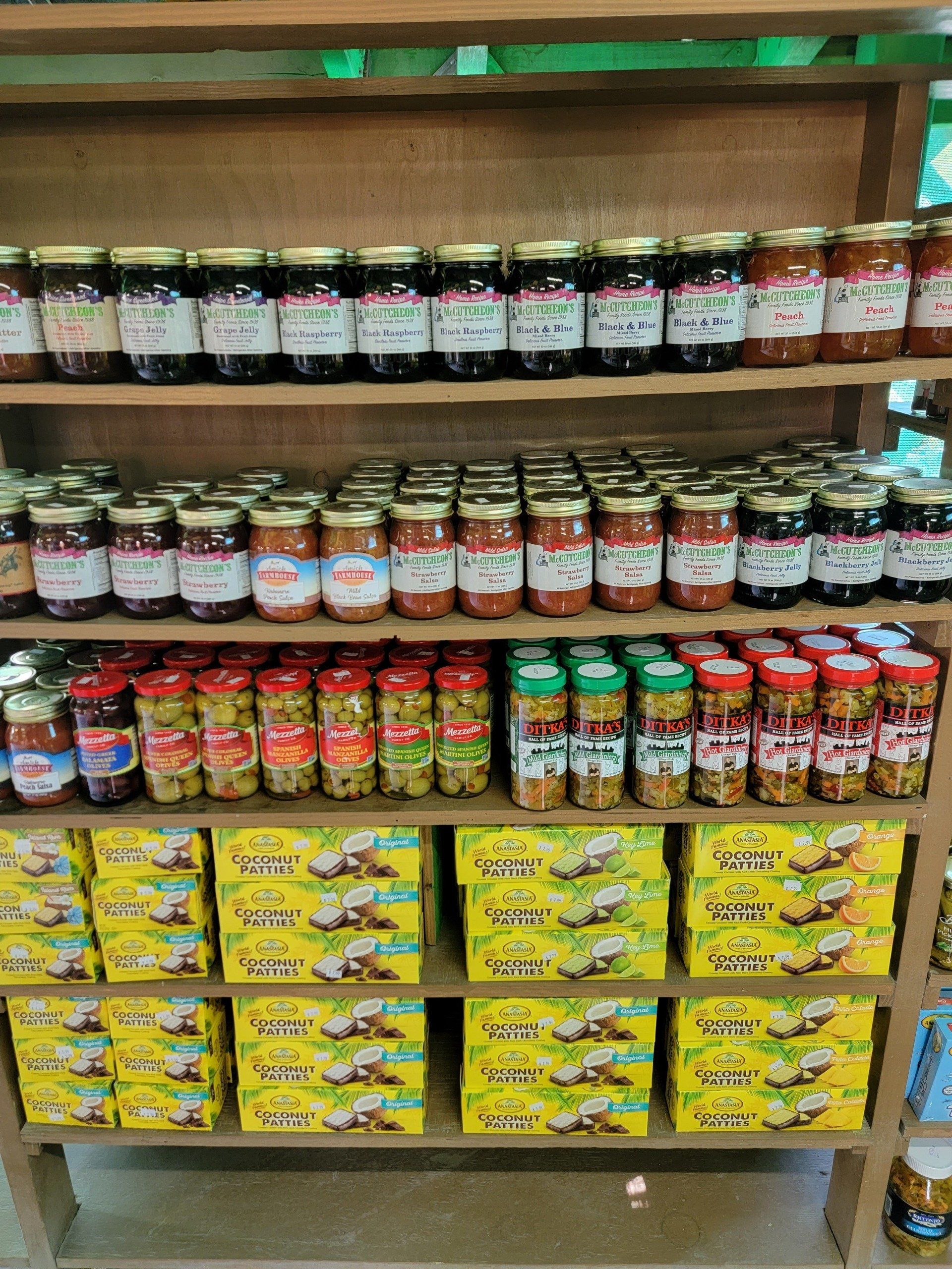 Shelves stocked with jars of preserves, olives, and boxes of crackers in a market setting.