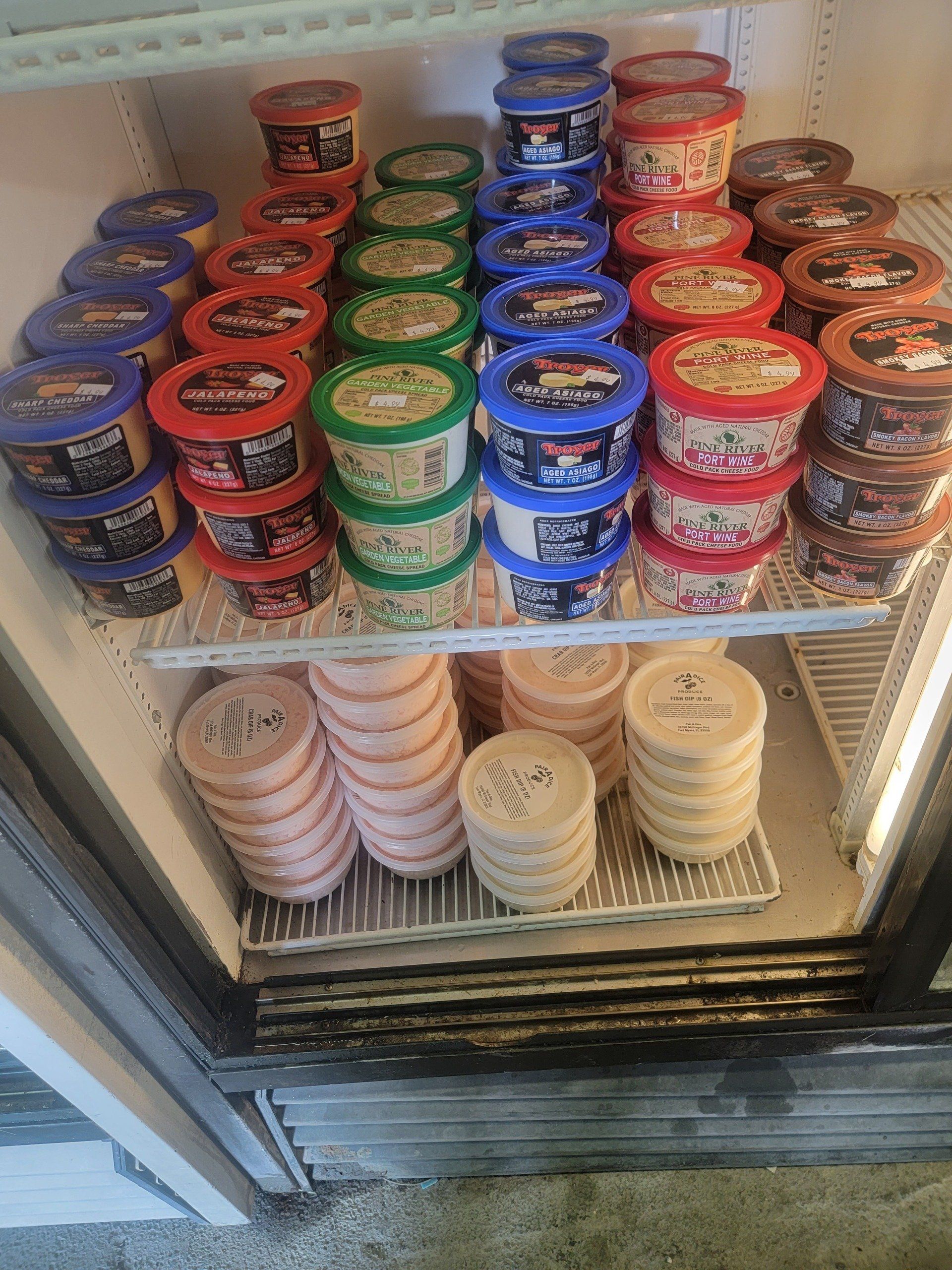 Refrigerator stocked with colorful tubs of dips and spreads.