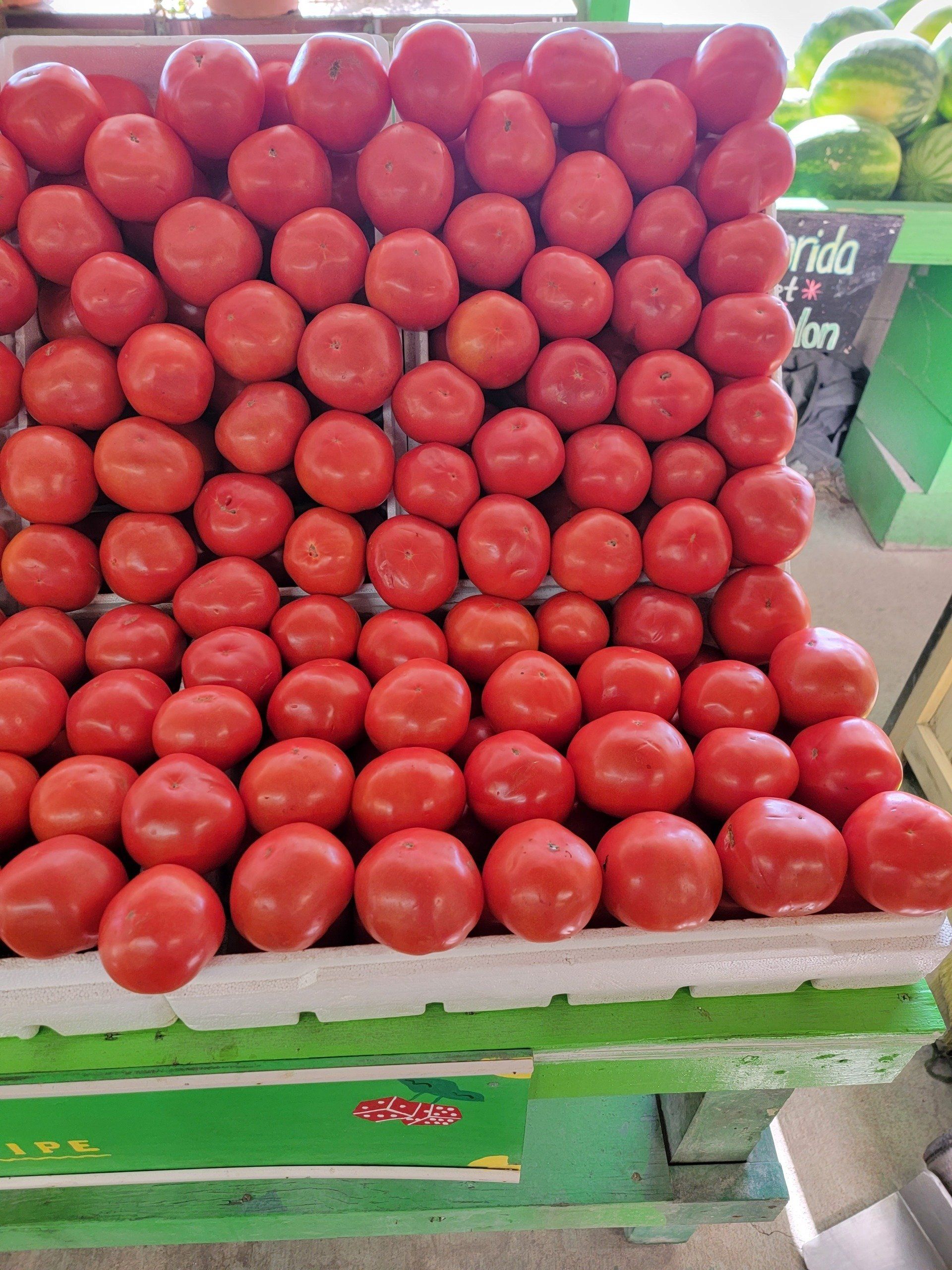 Display of ripe red tomatoes on a white foam tray at a produce stand.